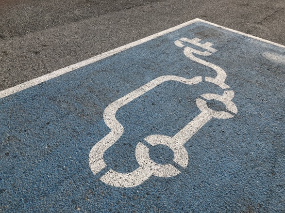 A blue parking space is marked with a white line drawing of an electric car and a charging plug, indicating a designated spot for electric vehicle charging.