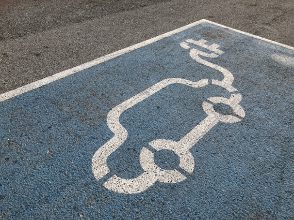 A blue parking space is marked with a white line drawing of an electric car and a charging plug, indicating a designated spot for electric vehicle charging.