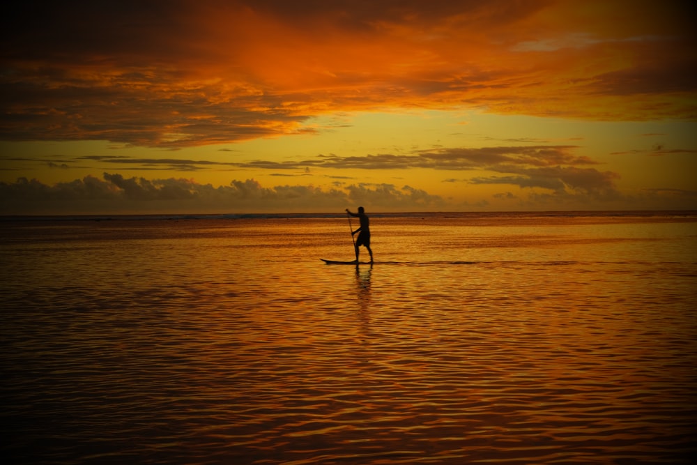 man in black shorts standing on paddle board during sunset