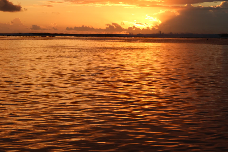 Serene sunset over water with cloud formation casting orange glow across the sky
