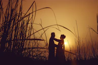 silhouette of man and woman standing on grass field during sunset