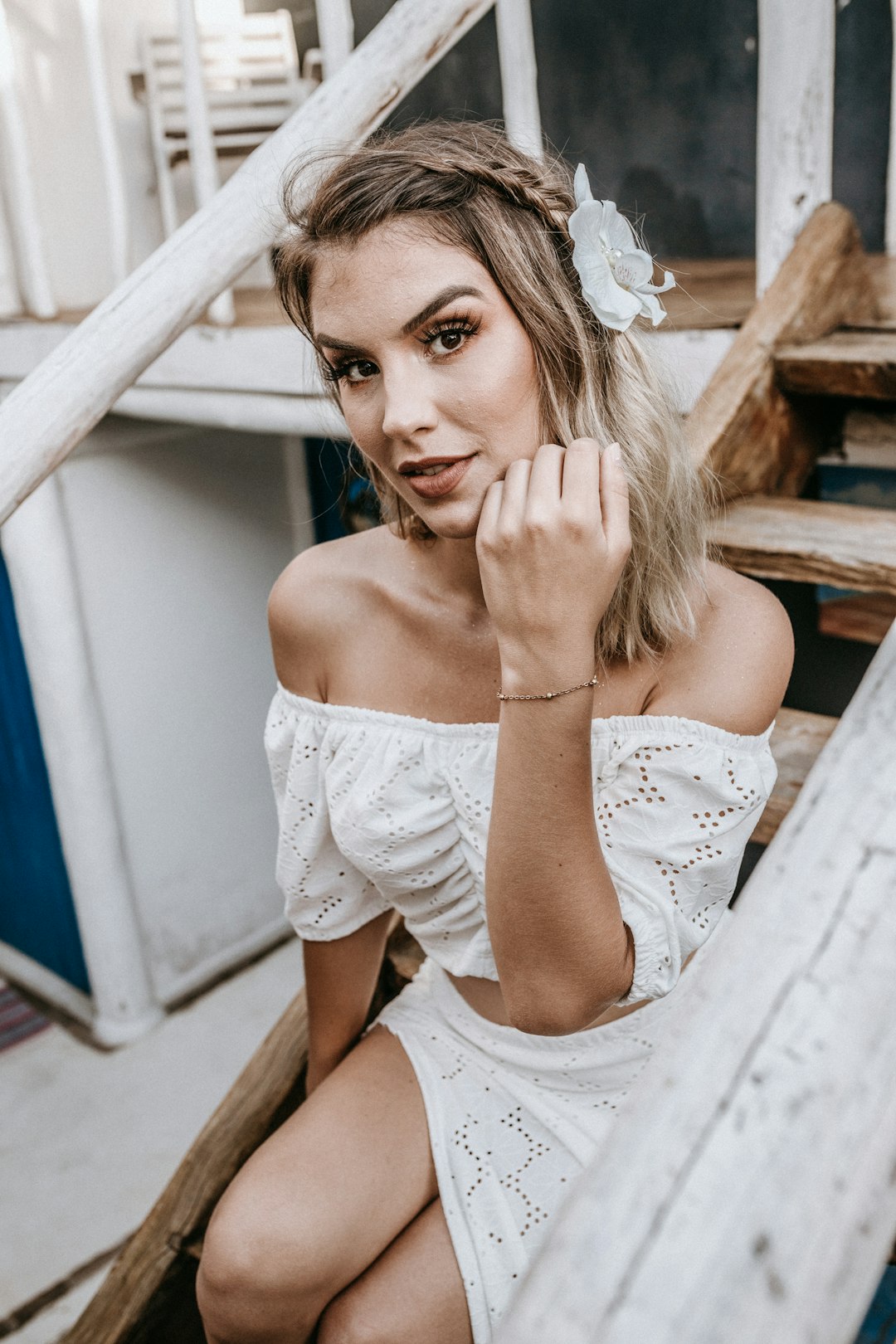 woman in white off shoulder dress sitting on brown wooden stairs