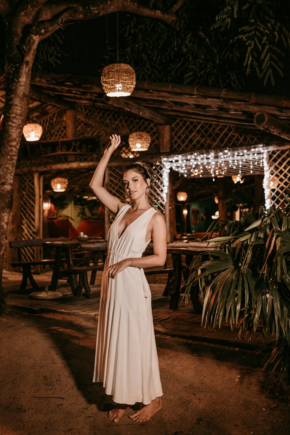 Mujer en vestido blanco sin mangas de pie cerca de la palmera durante la noche