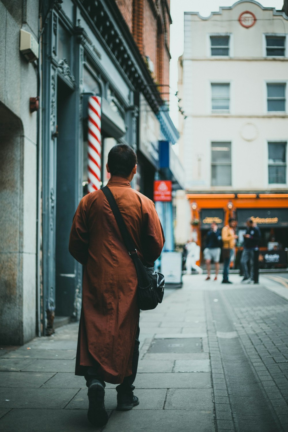 man in brown coat walking on sidewalk during daytime