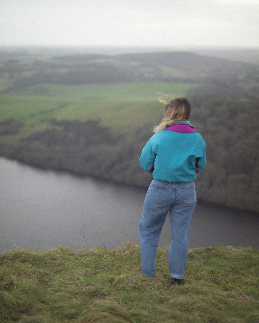 woman in blue denim jeans standing on green grass field near lake during daytime