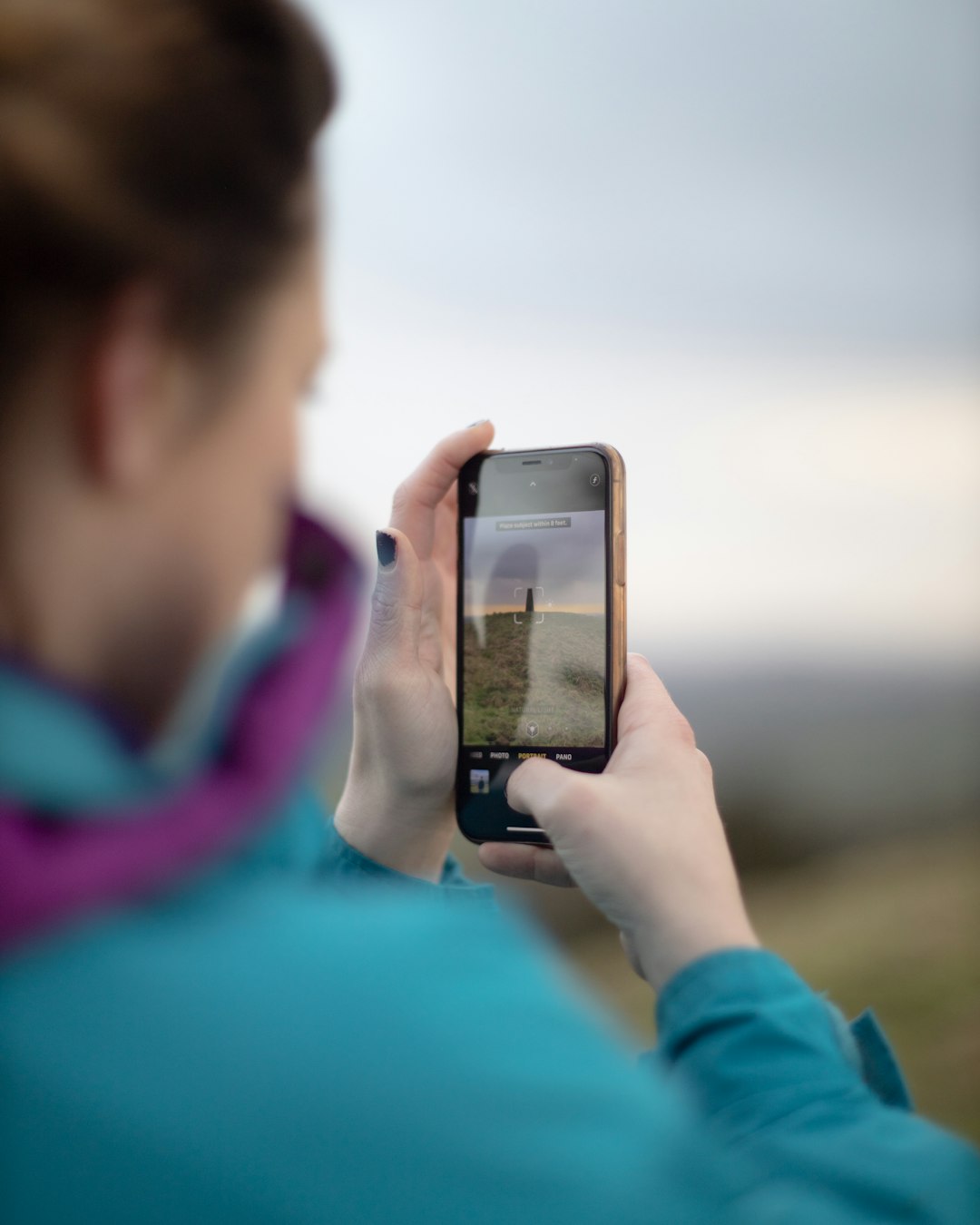 person in teal long sleeve shirt holding silver iphone 6