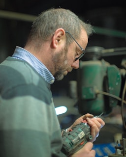 man in gray collared shirt wearing black framed eyeglasses holding smartphone