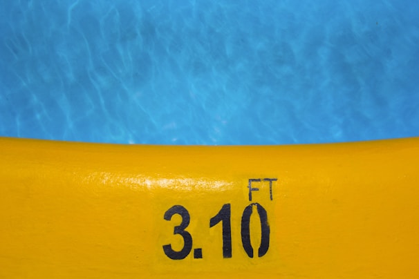 A bright yellow pool edge with the depth marking of 3.10 feet written in black. The blue pool water contrasts against the yellow edge, showing ripples and reflections.