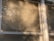Sunlight filters through partially closed blinds, casting warm shadows on the window frame. A delicate lace curtain peeks through the slats, adding a touch of decorative detail.