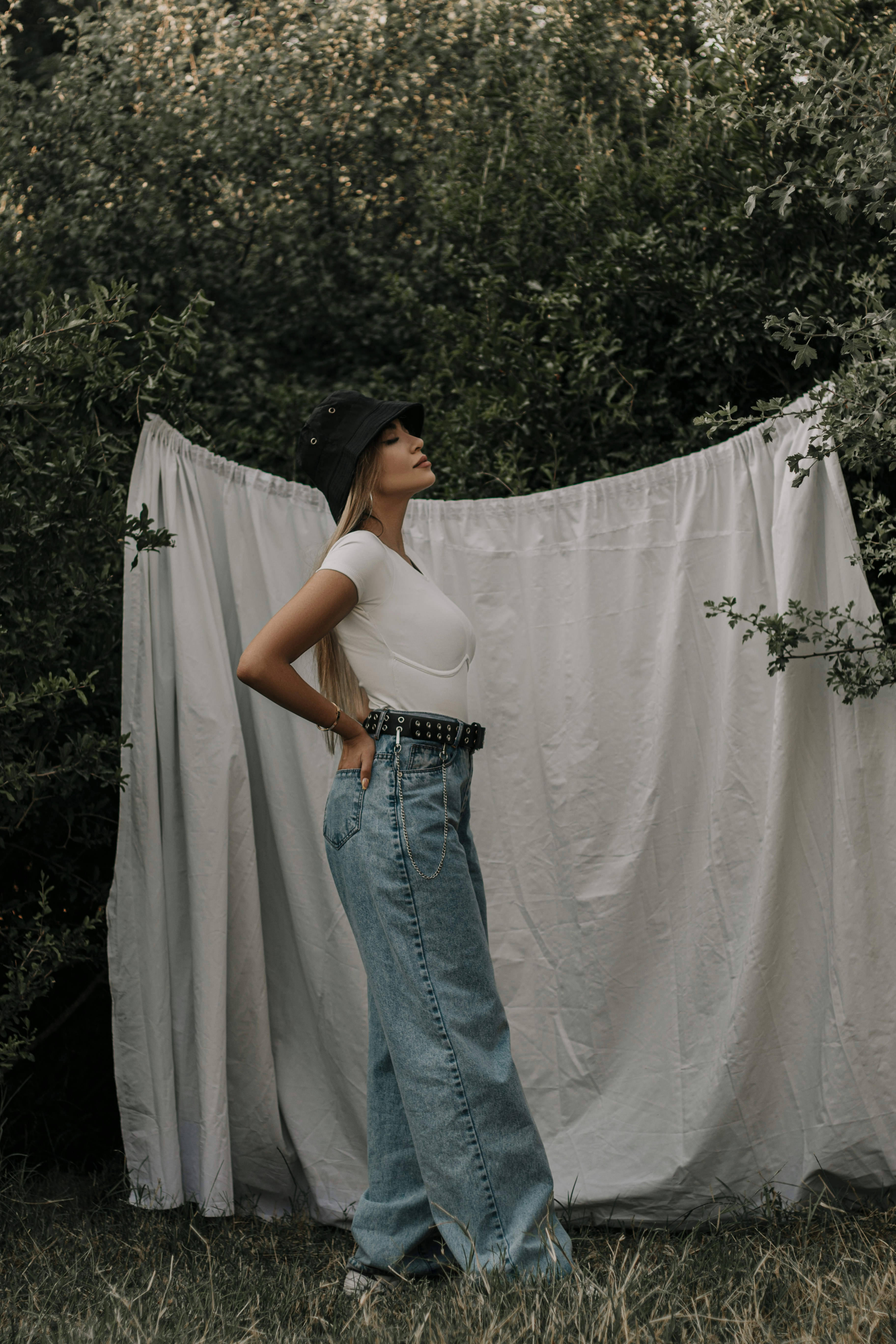 woman in white tank top and blue denim jeans standing beside white textile