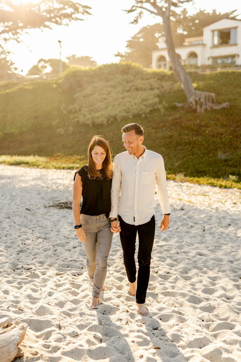 man in white dress shirt standing beside woman in black tank top on white sand during