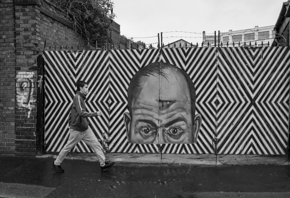 grayscale photo of man in stripe shirt standing beside wall