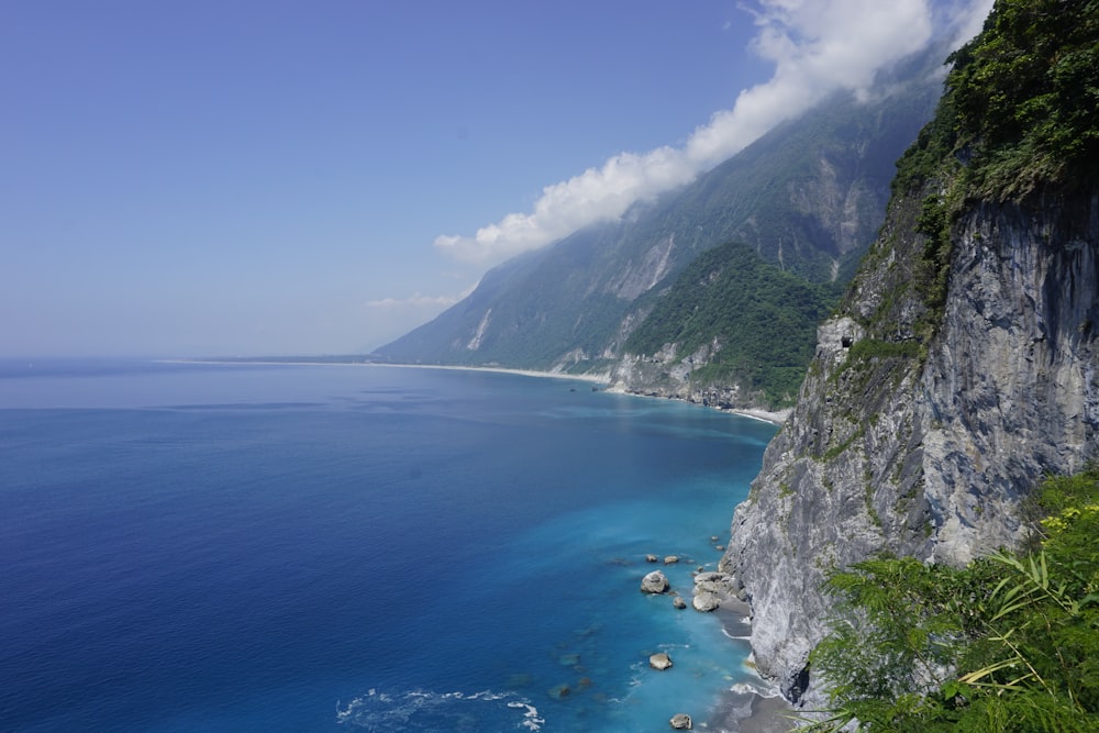 montanha verde e cinza ao lado do mar azul sob o céu azul durante o dia