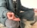 A person sits cross-legged on a soft, textured surface, wearing a knitted sweater and pants. The focus is on their hand, which is placed on one knee in a meditative pose, with fingers delicately creating a mudra.