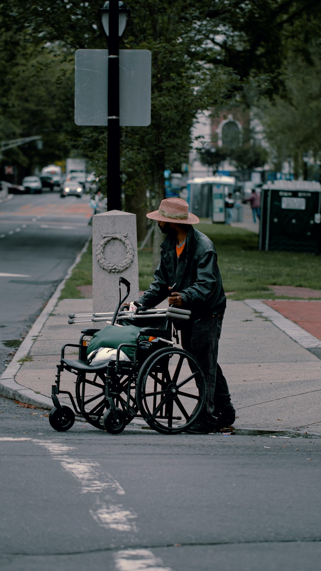 man in black jacket and brown hat riding on black and green wheel chair on sidewalk