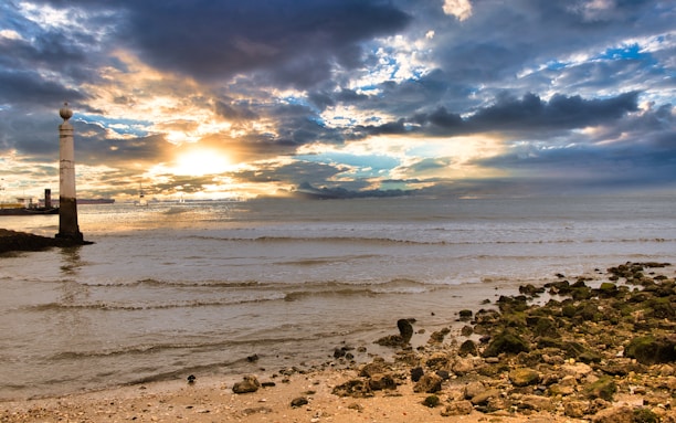A serene view of Portugal’s Silver Coast with golden sandy beaches and a lighthouse at sunset.