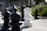 An outdoor giant chess set with prominently featured black and white pawns and other pieces on a concrete surface. The background includes blurred greenery and a building, suggesting a garden or park setting.