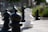 An outdoor giant chess set with prominently featured black and white pawns and other pieces on a concrete surface. The background includes blurred greenery and a building, suggesting a garden or park setting.