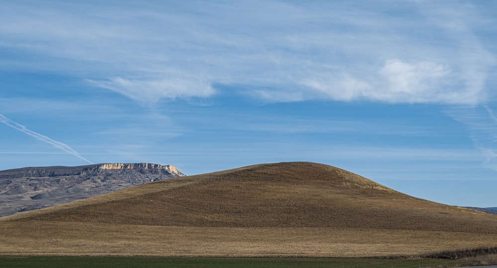 green grass field near mountain under blue sky during daytime