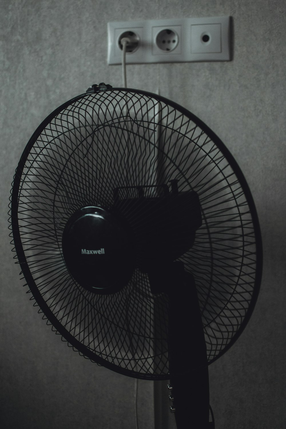 black pedestal fan turned on near white wall