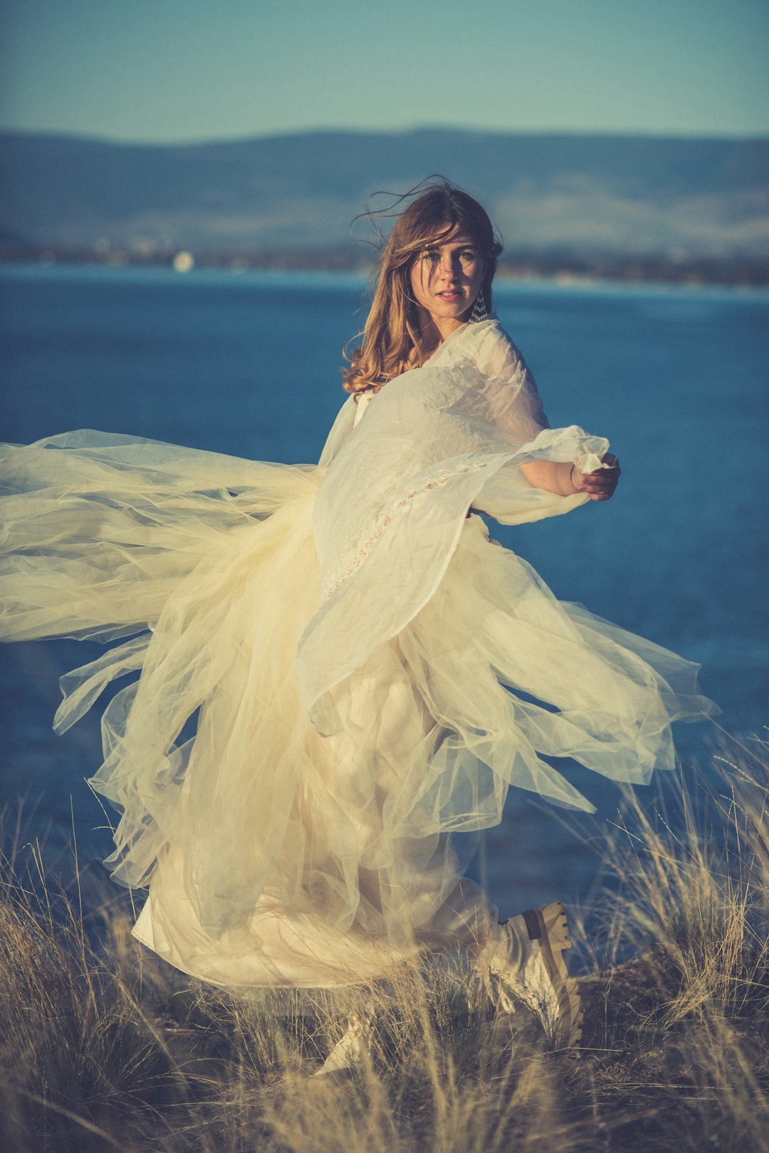 woman in white dress standing on brown grass field near body of water during daytime