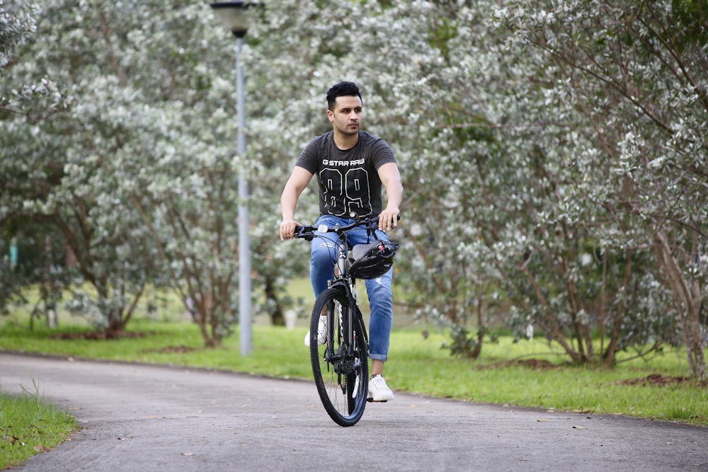 Uomo in t-shirt nera e jeans blu in denim che va in bicicletta durante il giorno