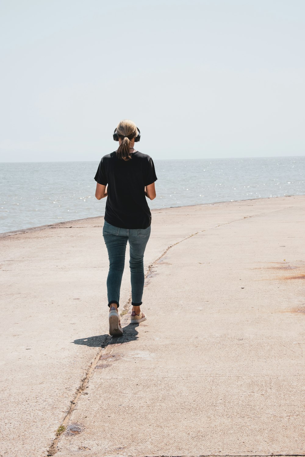 woman in black jacket and blue denim jeans standing on beach shore during daytime