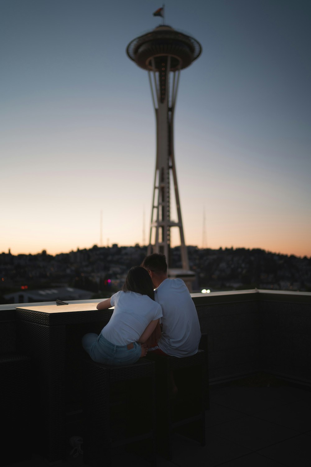 man and woman sitting on the roof of a building during sunset
