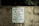 A worn concrete wall displays a sign listing park regulations, including operation hours from daylight to dusk and prohibitions against alcohol, skateboarding, littering, rollerblading, camping, and disorderly conduct. The sign emphasizes that violators will face prosecution.