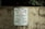 A worn concrete wall displays a sign listing park regulations, including operation hours from daylight to dusk and prohibitions against alcohol, skateboarding, littering, rollerblading, camping, and disorderly conduct. The sign emphasizes that violators will face prosecution.