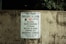 A worn concrete wall displays a sign listing park regulations, including operation hours from daylight to dusk and prohibitions against alcohol, skateboarding, littering, rollerblading, camping, and disorderly conduct. The sign emphasizes that violators will face prosecution.