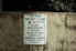 A worn concrete wall displays a sign listing park regulations, including operation hours from daylight to dusk and prohibitions against alcohol, skateboarding, littering, rollerblading, camping, and disorderly conduct. The sign emphasizes that violators will face prosecution.