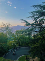 A panoramic view of a convoy of motorcycles winding through lush green hills under clear blue skies.