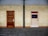 Two doors side by side on a tiled wall, one brown and the other white. The wall is tiled with yellowish rectangular tiles. The ground is paved with gray stone tiles, and a vertical metal beam separates the two doors.