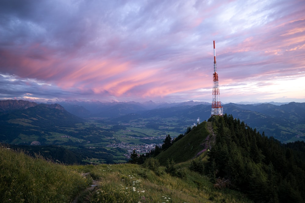 red and white tower on top of green mountain under cloudy sky during daytime