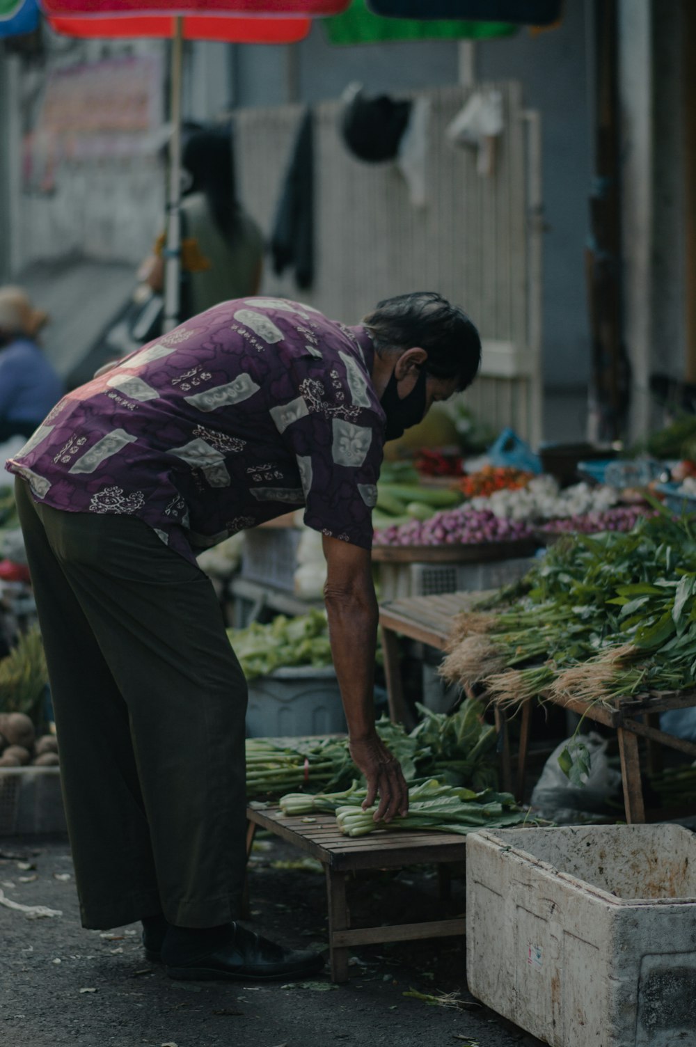 man in purple and white floral shirt and black pants standing on brown wooden plank