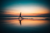 silhouette of person standing on seashore during sunset