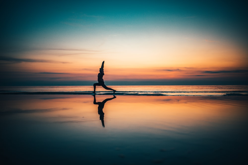 silhouette of person standing on seashore during sunset