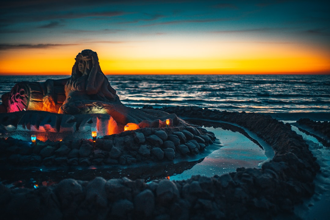 woman in black jacket sitting on rock formation near sea during sunset