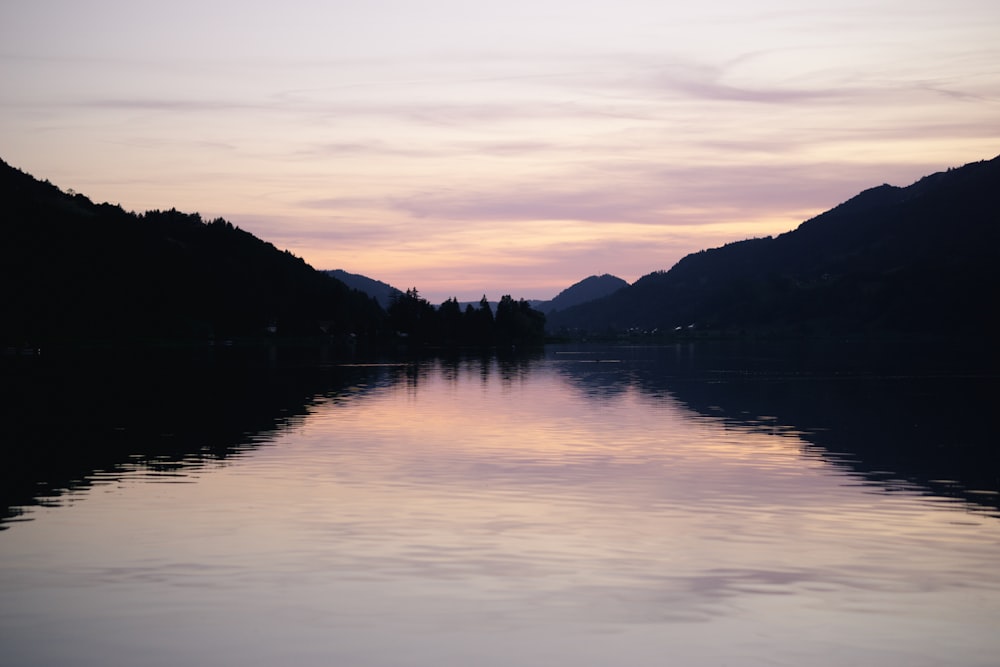 silhouette of mountain near body of water during sunset