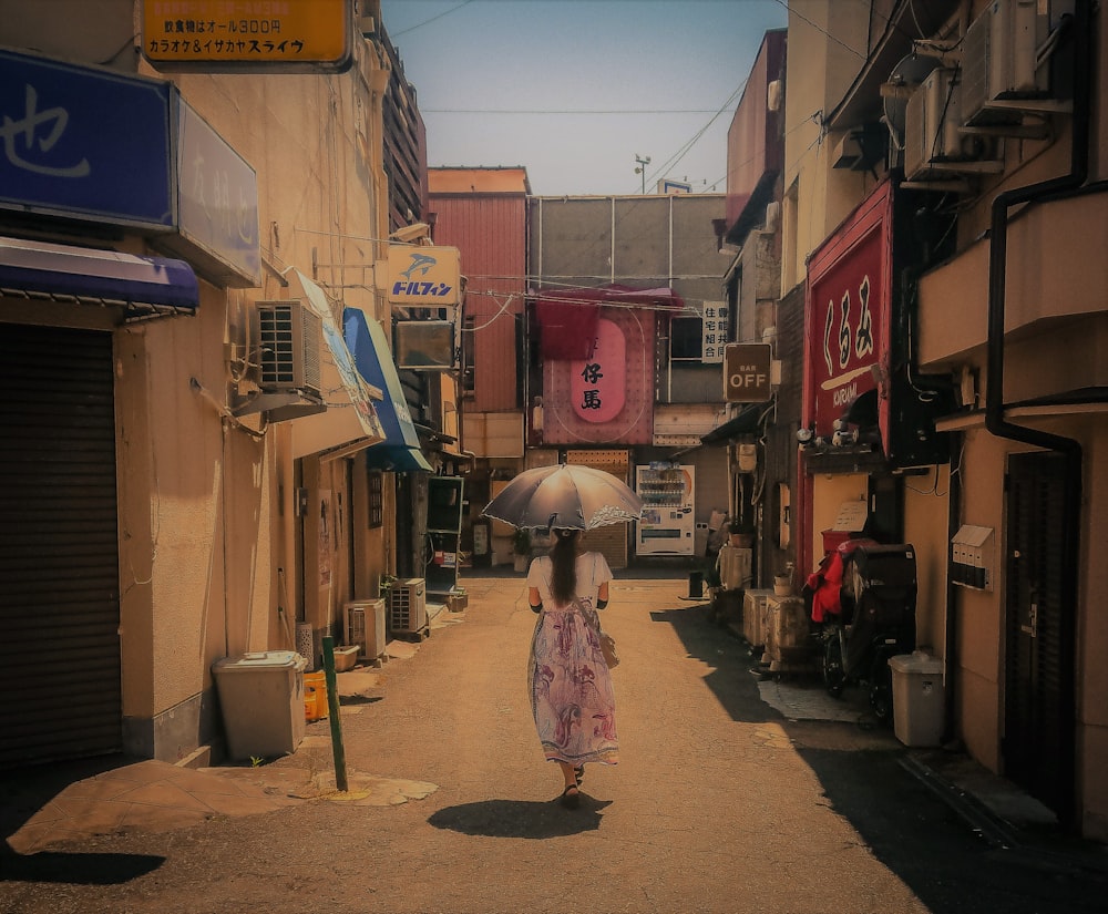 woman in pink dress holding umbrella walking on sidewalk during daytime