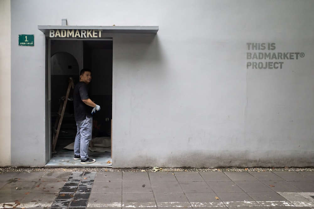 man in black t-shirt and blue denim jeans standing near gray concrete wall