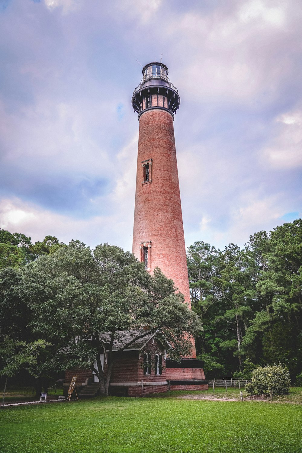 brown and black concrete lighthouse near green trees under white clouds and blue sky during daytime