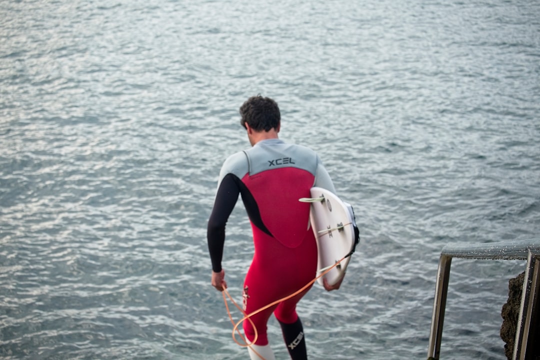 man in black and red wet suit holding white and red surfboard