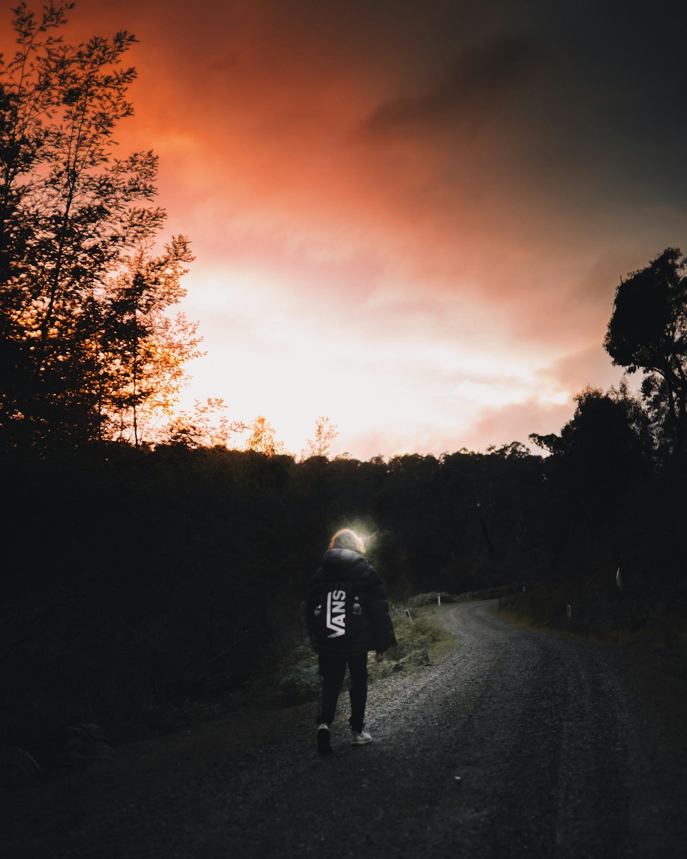 homme en veste noire marchant sur la route au coucher du soleil