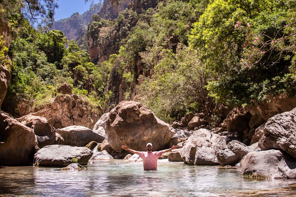 person in pink shirt sitting on rock in river during daytime