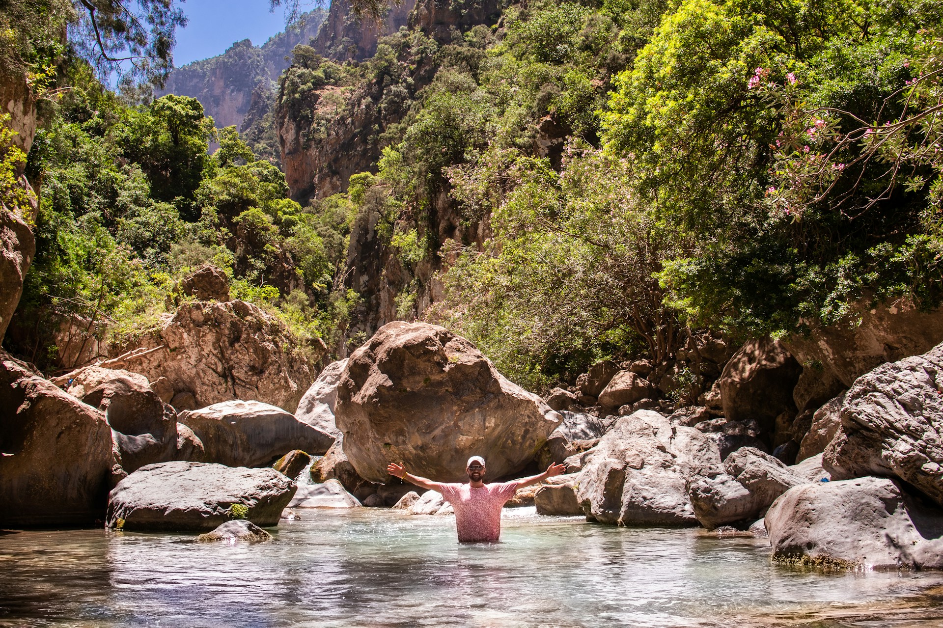 person in pink shirt sitting on rock in river during daytime