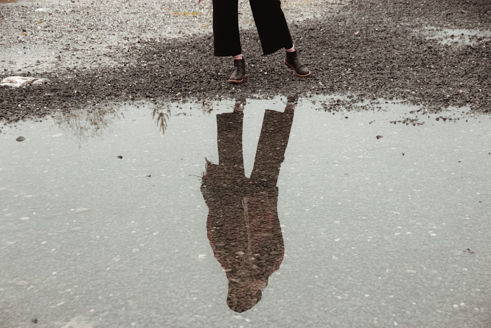 Person in schwarzen Hosen und braunen Stiefeln auf grauem Betonboden stehend