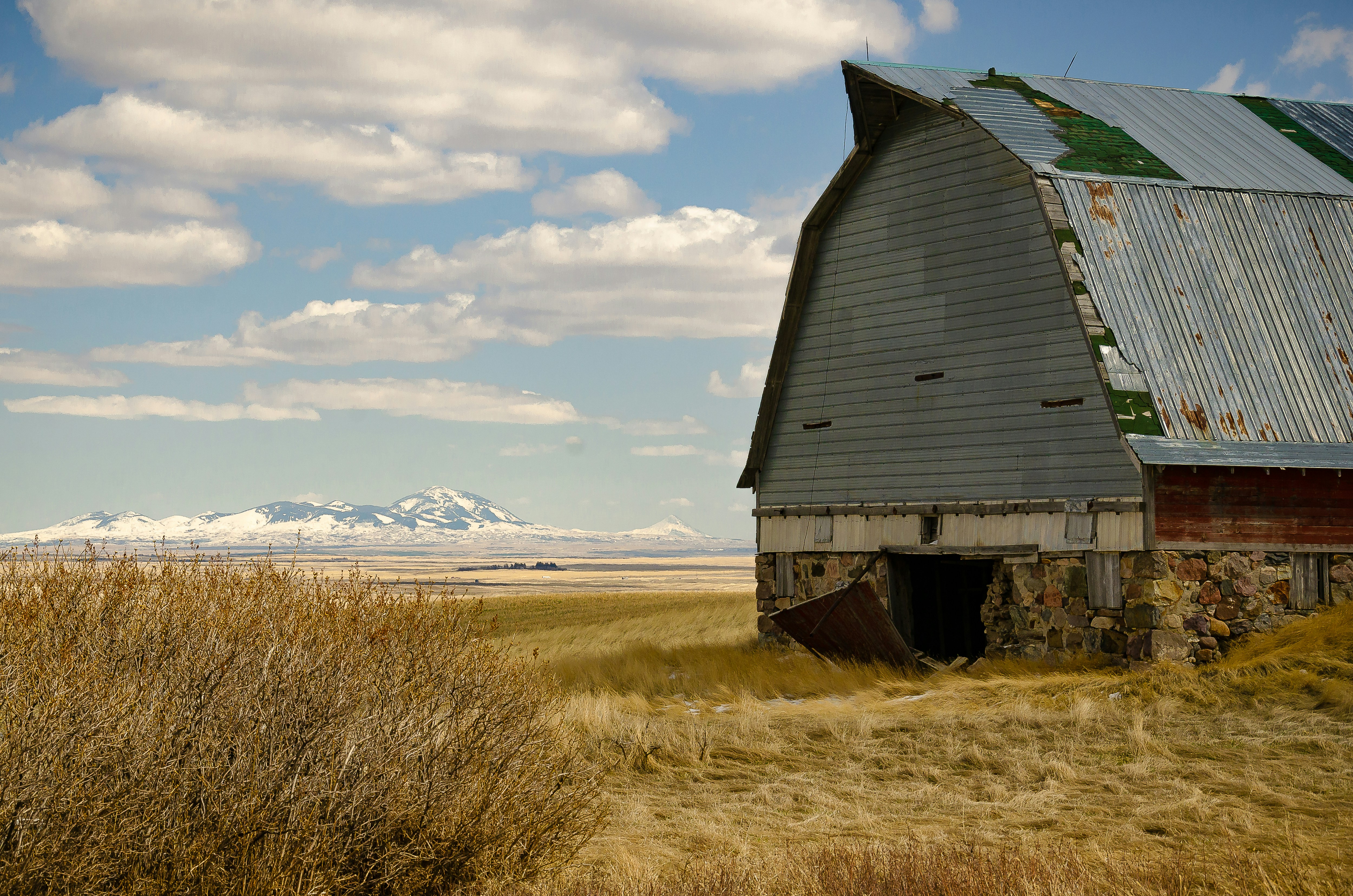 Brown wooden barn on brown grass field under white clouds and blue sky ...