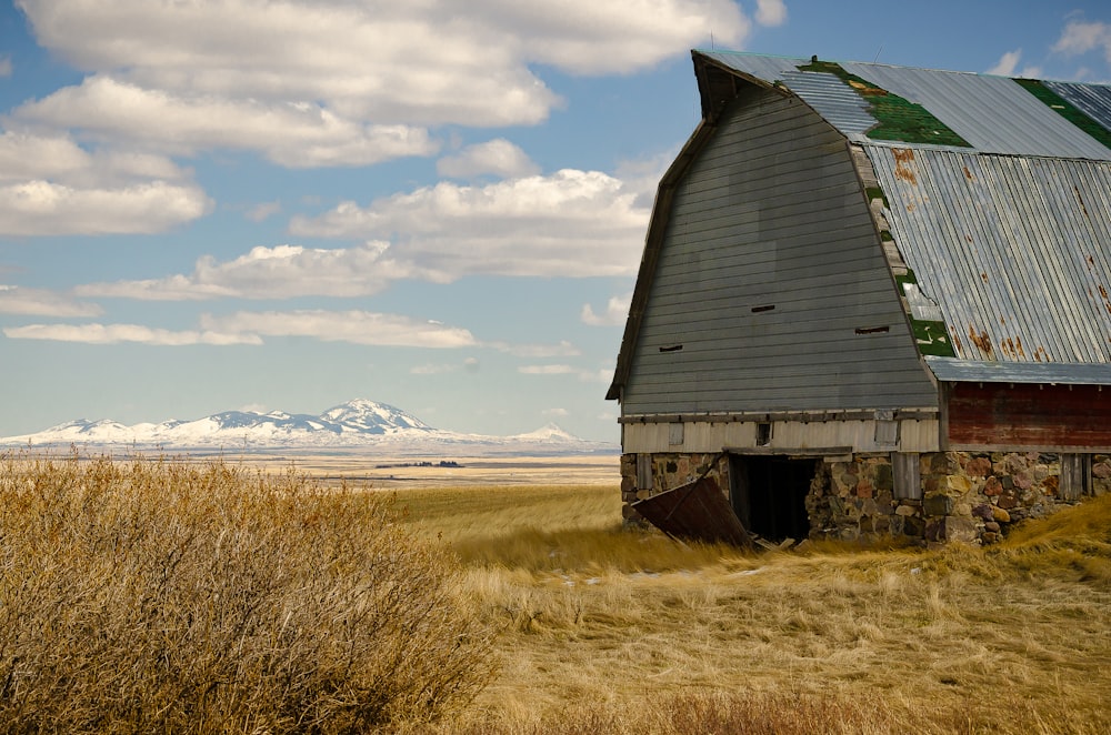 brown wooden barn on brown grass field under white clouds and blue sky during daytime